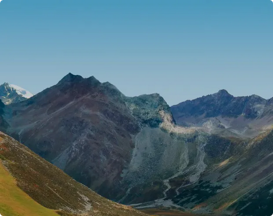 Berglandschaft in den Alpen mit einem Pfad, der durch grüne und felsige Hügel führt, vor einem klaren blauen Himmel