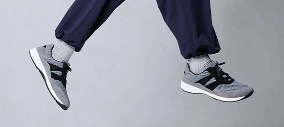 Ein Paar graue und schwarze Sportschuhe beim Springen, getragen von einer Person in blauen Hosen