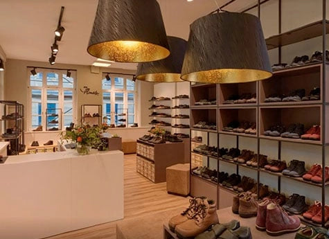 Innenansicht eines modernen Schuhgeschäfts mit Pflanzen, Regalen voller Schuhe und großer Beleuchtung.