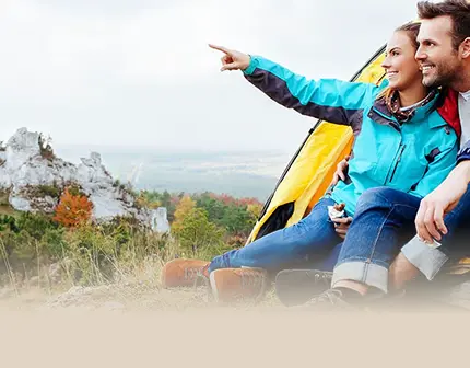 Lächelndes Paar sitzt vor Zelt in den Bergen und blickt in die Ferne. Text: Die Berge rufen! BÄR Wanderschuh Kaufberatung.