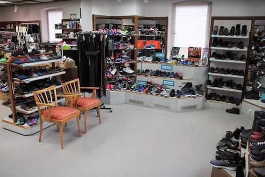 Innenansicht eines Schuhgeschäfts mit einer großen Auswahl an Sportschuhen, Regalen voller Schuhe und Accessoires sowie zwei Stühlen im Vordergrund.